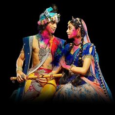 two people dressed in colorful costumes sitting next to each other on a black background,