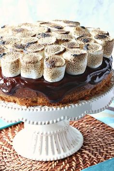 a cake with chocolate frosting and marshmallows on top sitting on a wicker place mat