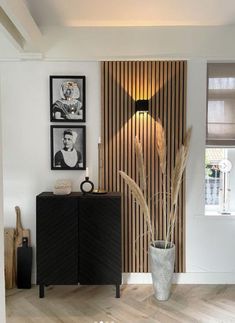 a vase with some plants in it next to a wooden paneled wall and pictures on the wall