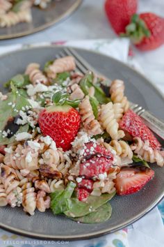 two plates with pasta salad and strawberries on them