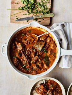 two bowls filled with stew and rice on top of a wooden table next to a cutting board