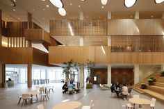 people are sitting at tables and chairs in a large room with wooden staircases on both sides