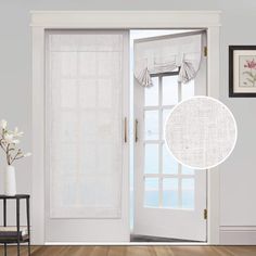 an open door with white curtains and flowers in the vase next to it on top of a hard wood floor