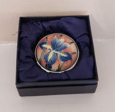 a blue and yellow flower brooch sitting in a black box on a white surface