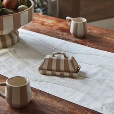 the table is set with two mugs and a bowl of fruit