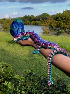 a person is holding a colorful dragon like object in their hand while standing on the grass