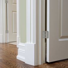 an open door on the side of a room with wood flooring and white trim