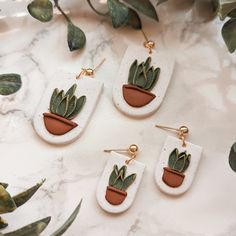 three pairs of plant shaped earrings sitting on top of a marble table next to plants