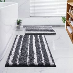 two bathroom rugs on the floor in front of a bathtub and shelf with towels