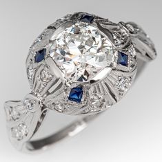 This circa 1930s Art Deco engagement ring is centered with a round old European cut diamond, weighing 0.97 carats, in a four-prong setting. The top of the ring features engraving and milgrain details and is bead set with eighteen (18) round single cut diamonds and four (4) bezel set, square mixed cut synthetic sapphires. The ring measures 11.1mm at the top, rises 6.1mm above the finger, tapering to 1.2mm wide and 0.7mm thick at the base of the shank. The ring is currently a size 5.25 and we offe Athena Jewelry, Mafia Princess, Filigree Engagement Ring, Princess Jewelry, Antique Diamond Rings, 1930s Art, Art Deco Engagement, Antique Engagement, 1930s Art Deco