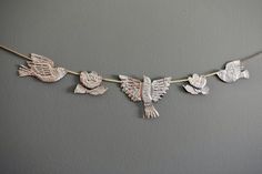 three birds are hanging on a string with leaves and flowers in the shape of doves