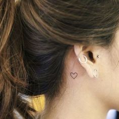 a woman wearing ear piercings with a heart tattoo on her left side of the ear