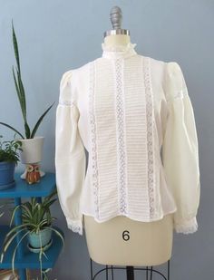 Vintage 80's Victorian blouse. Off white silk with high lace ruffle collar, eyelet lace, horizontal pleats and button lace cuffs. Button down back with billowy long sleeves with puffed shoulders. Sightly sheer overall. Straight hem. Gorgeous top would be great for a formal event.  Fits up to a size large. Please double-check the measurements below: MEASUREMENTS--Taken with garment laying flat, in inches, doubled: Bust: 40"  Waist: 38"  Shoulder: 14" Length: 23" {top neck to bottom hem} Neck: 14" Sleeve length: 24.5" Label/ Era: Royal Silk | 1980 Stated Size: 8 Fabric: Silk, acrylic buttons Condition: Excellent condition. Freshly laundered. No known issues.  ★ Shop entire shop here: https://www.etsy.com/shop/retrosuzysvintage Instagram | retrosuzysvintage Facebook | retrosuzysvintage Pinter Victorian Blouse, Lace Cuffs, Ruffle Collar, Eyelet Lace, Lace Ruffle, White Silk, Lace Blouse, Silk Blouse, Formal Event