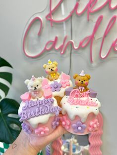 a hand holding up a small cake with teddy bears on it's top and the words happy birthday written in large letters