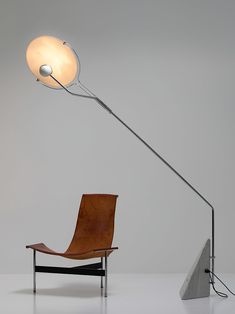 a chair sitting next to a floor lamp on top of a white table with a gray background