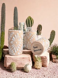 some cactus plants are sitting next to each other in front of a pink wall and two white vases