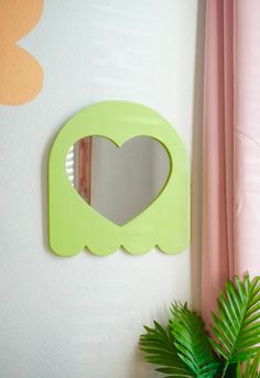 a green heart shaped mirror mounted to the side of a wall next to a potted plant