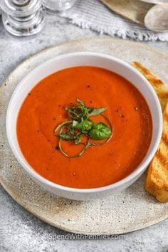 a bowl of tomato soup on a plate next to some toasted bread and water