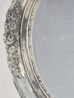 an ornate silver framed mirror with flowers on the rim and bottom edge, against a white background