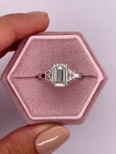 a woman's hand holding an engagement ring in a pink velvet box with diamond accents