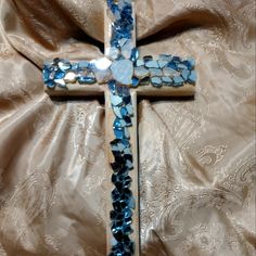 a cross made out of blue glass beads on a tan cloth with a gold background