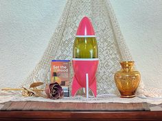 a pink rocket ship sitting on top of a table next to a vase and other items