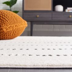 a white rug with black dots on it in front of a brown dresser and television