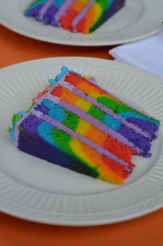 two white plates topped with slices of cake covered in rainbow colored frosting on an orange table cloth