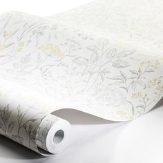 a white wallpaper with yellow flowers and leaves on it's side, next to a roll of toilet paper