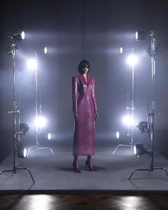 a woman in a purple leather dress standing on a stage surrounded by lights and lighting equipment