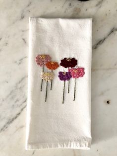 three flowers embroidered onto a white towel on a marble countertop with a black object in the background