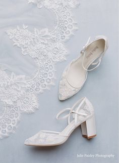 two pairs of white wedding shoes sitting on top of a blue surface next to lace