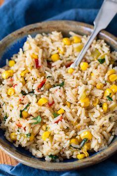 a bowl filled with rice and corn on top of a blue cloth next to a fork