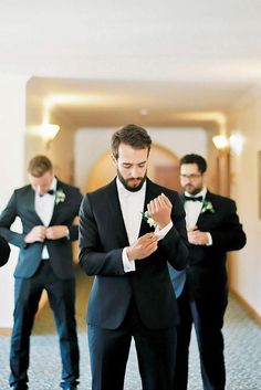 a man in a tuxedo is adjusting his tie while another man looks on