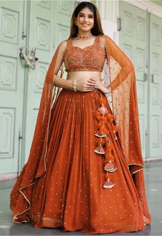 Faux Georgette Lehenga in Orange This attire with Cotton and Shantoon Lining is Enhanced with Fancy Tassels, Resham, Thread, Zari and Sequins Work Available with a Unstitched Faux Georgette Orange Choli and a Faux Georgette Dupatta in Orange The Semi-Stitched Lehenga Waist and Hips are Customizable from 24 to 62 inches and from 28 to 66 inches respectively and Lehenga Length is 38 to 42 inches Do Note: Accessories shown in the image are for presentation purposes only. (Slight variation in actual Georgette Embroidery Lehenga, Orange Lehenga Choli, Choli Designs For Marriage, Orange Chaniya Choli For Navratri, Crop Blouse Designs For Lehenga, Terracotta Lehenga, Lehenga Models For Stitching, Orange Traditional Outfits, Mehendi Look For Bridesmaid