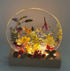 a glass bowl filled with lots of different types of flowers and leaves on top of a wooden block