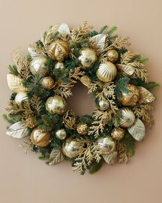 a christmas wreath hanging on the wall with gold ornaments and greenery around it's edges