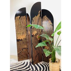 three wooden art pieces sitting on top of a zebra print rug next to a potted plant