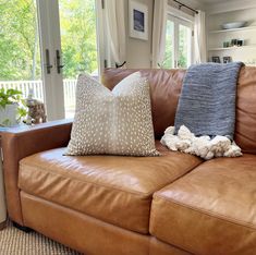 a brown leather couch with two pillows on it's back and a window in the background