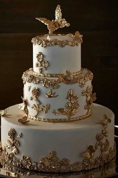 a three tiered white wedding cake with gold decorations