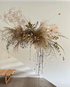 an arrangement of dried flowers hanging from the ceiling in a white room with a wooden bench