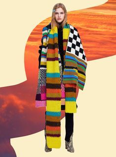 a woman standing in front of an orange sky wearing a multicolored knitted scarf