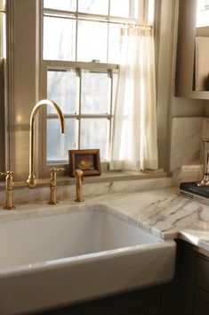 a white sink sitting under a window next to a counter top with a faucet