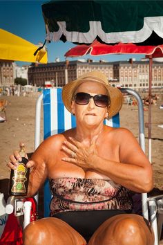 an older woman sitting in a chair on the beach with her hands clasped to her chest