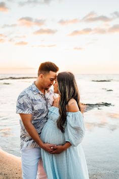 a pregnant couple standing next to each other on the beach at sunset with the ocean in the background