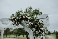 an outdoor wedding ceremony setup with white and pink flowers on the arborette, along with greenery