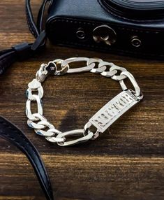 "This incredible men's bracelet has a figaro chain link (one oval link with three round links) and a satin finished plate in the center. The name in the center is cut out and raised. The bracelet has an easy lobster claw lock. It's the perfect, luxurious gift for someone special or for yourself.  We are currently offering this bracelet in the font shown in the sample. Bracelet length - 9\" Each of these pieces are custom made by hand. Depending on how many letters are in the name and what size the letters are, there can be slight variations on appearance. Please ask all questions before purchase as custom items are finale sale." Figaro Bracelet, Monogram Earrings, Monogram Bracelet, Medical Bracelet, Monogram Ring, Figaro Chain, Id Bracelets, Men's Bracelet, Disc Necklace