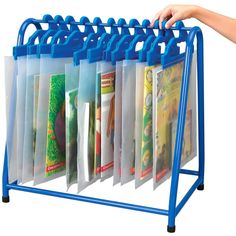 a person is holding up a blue rack with magazines on it and two hands are reaching for the folders