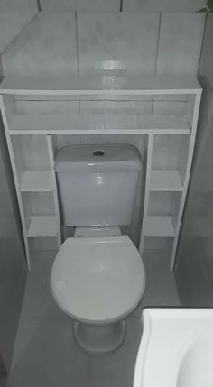 a white toilet sitting next to a sink in a bathroom under a shelf with shelves