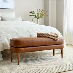 a leather bench sitting on top of a rug in front of a bed with white sheets and pillows